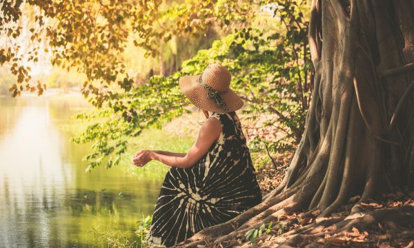 A young woman is sitting under a tree by the river